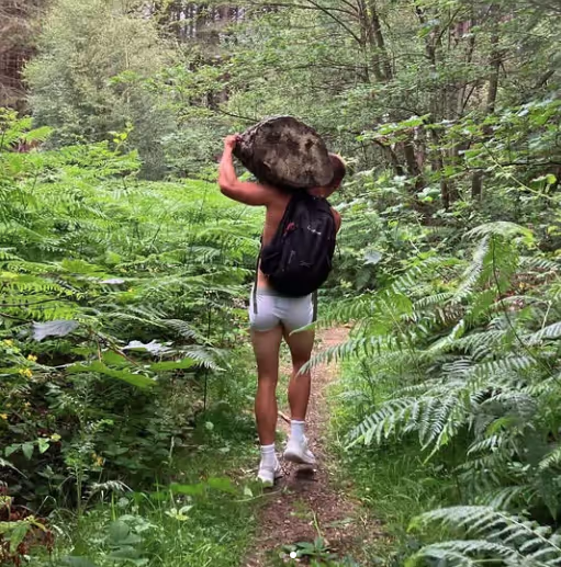 Damien Goring Personal Trainer showing his strength carring a rock in an English forest.